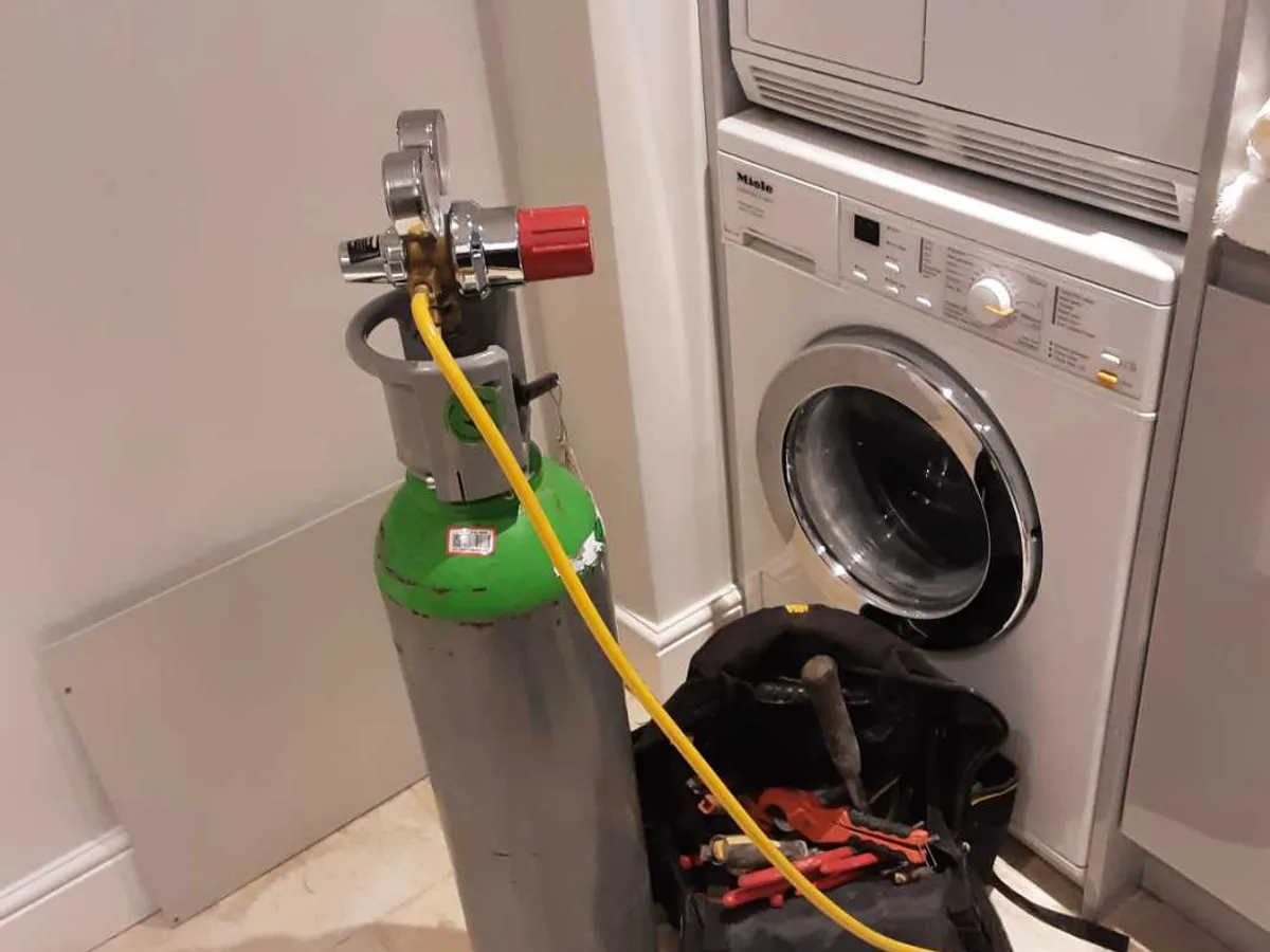 tracer gas cylinder with regulator and yellow hose connected to pipework during leak detection