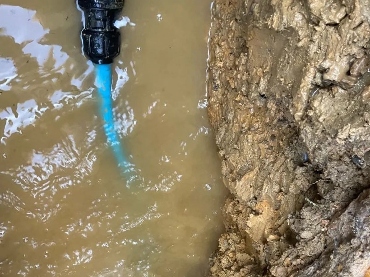 leak found at new blue MDPE pipe end with water flowing into flooded excavation