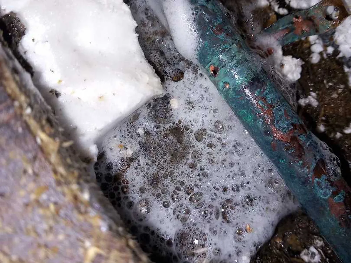 leak located at heavily corroded copper pipe beneath kitchen floor with water and foam present