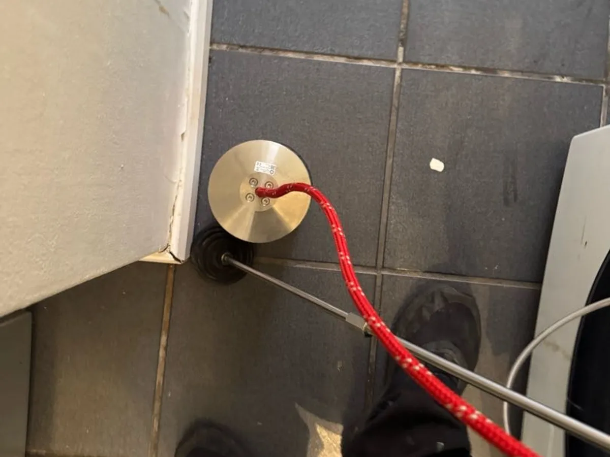 tracer gas detection probe inserted through kitchen floor tile during leak detection