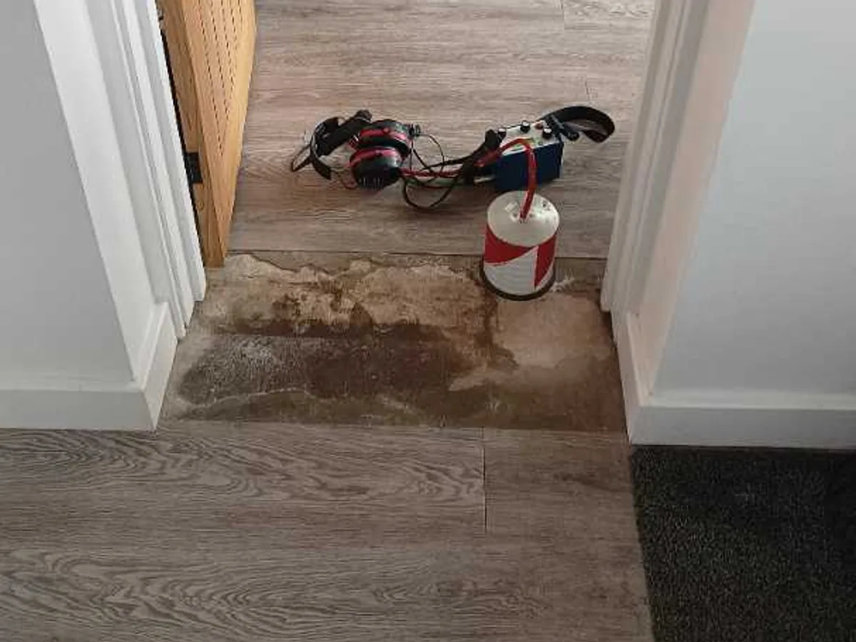 acoustic headset and tracer gas detector on damp kitchen threshold floor during leak detection