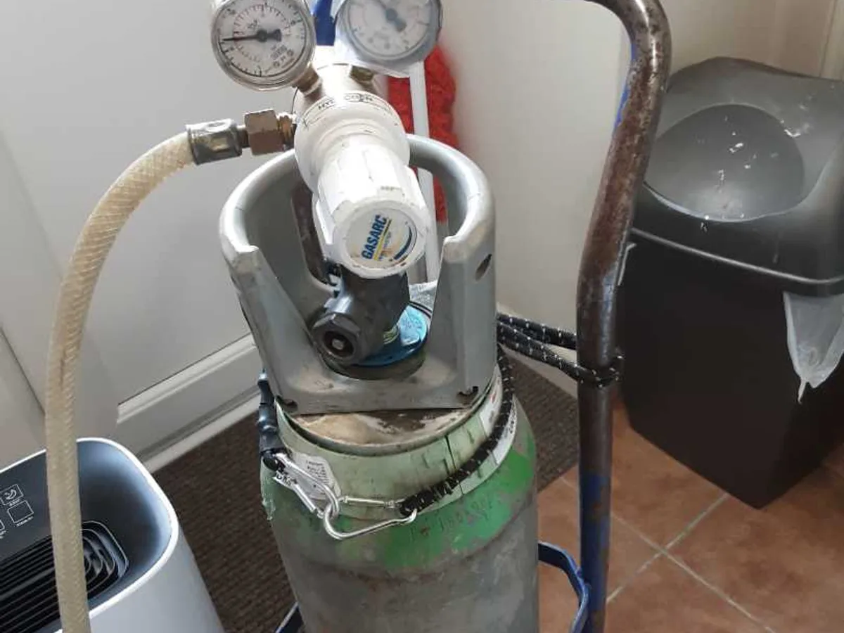 tracer gas cylinder with pressure gauges set up in kitchen during leak detection