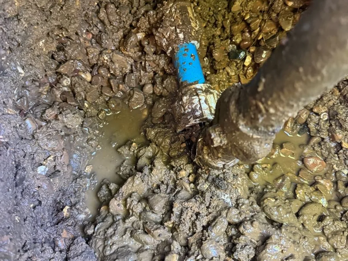 leak located at corroded plastic fitting on underground mains pipe in waterlogged excavation