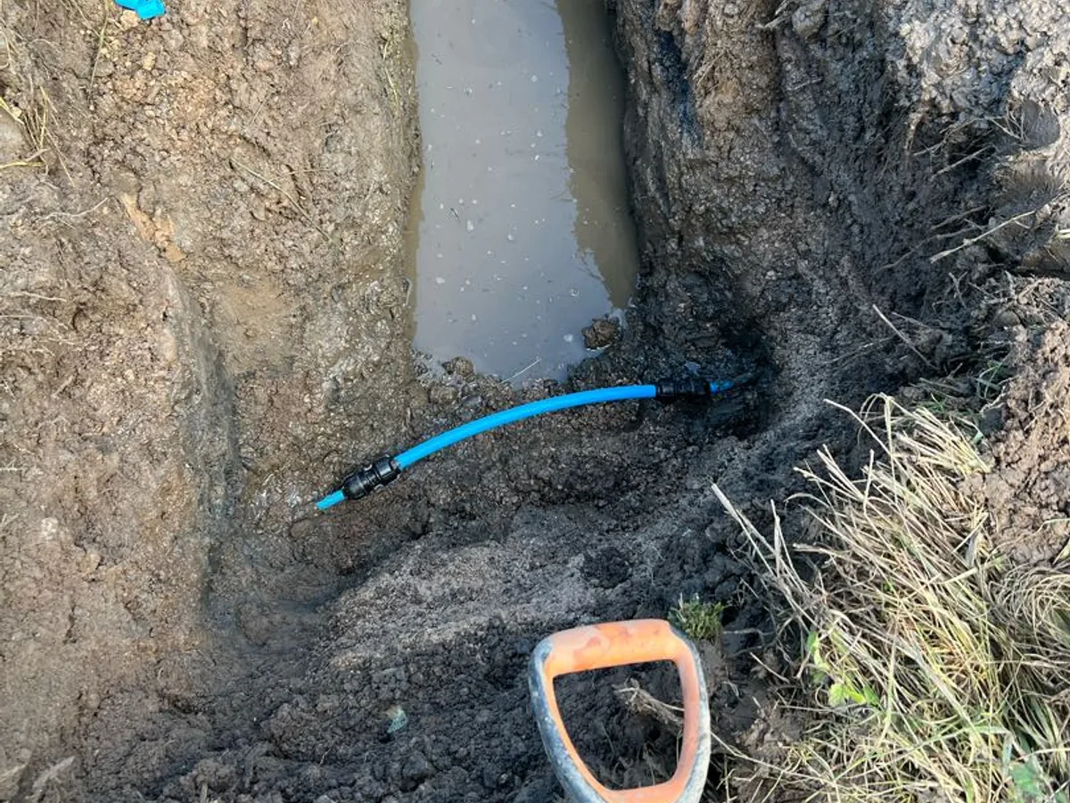 new blue MDPE pipe section with push-fit connector installed as repair completed in excavated trench