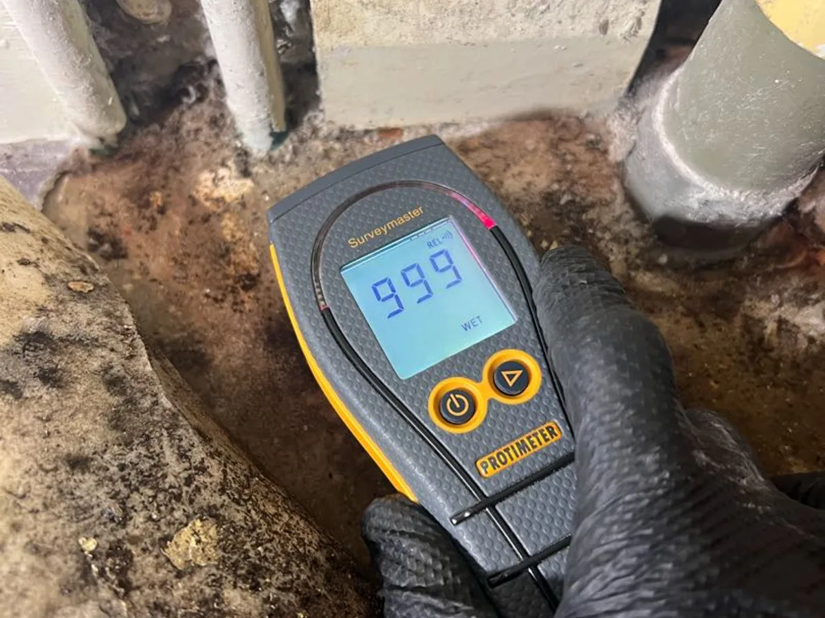 moisture meter displaying maximum reading of 999 WET at floor level during leak detection