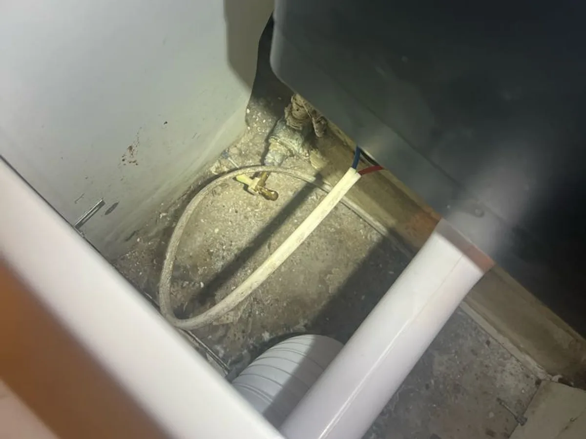 pipework and fittings beneath kitchen appliance exposed during leak detection investigation