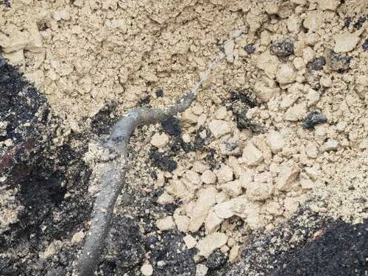 leak located beneath excavated tarmac patch in courtyard revealing sandy subsoil — leak located at