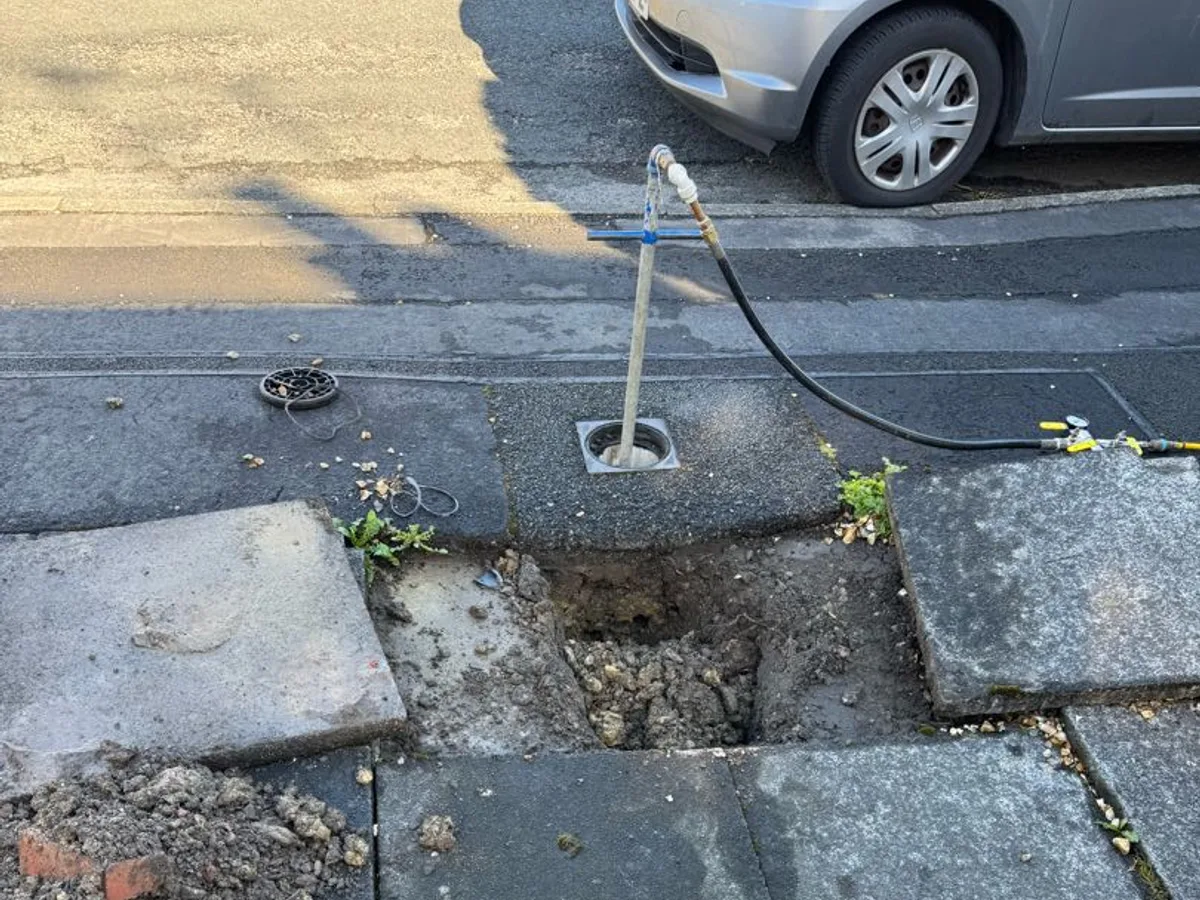 excavated hole in driveway with tracer gas probe inserted during leak detection investigation