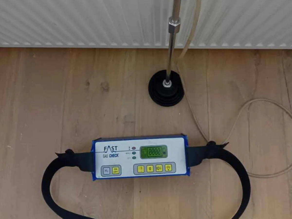 tracer gas detector probe placed at floor level beside radiator during leak detection survey