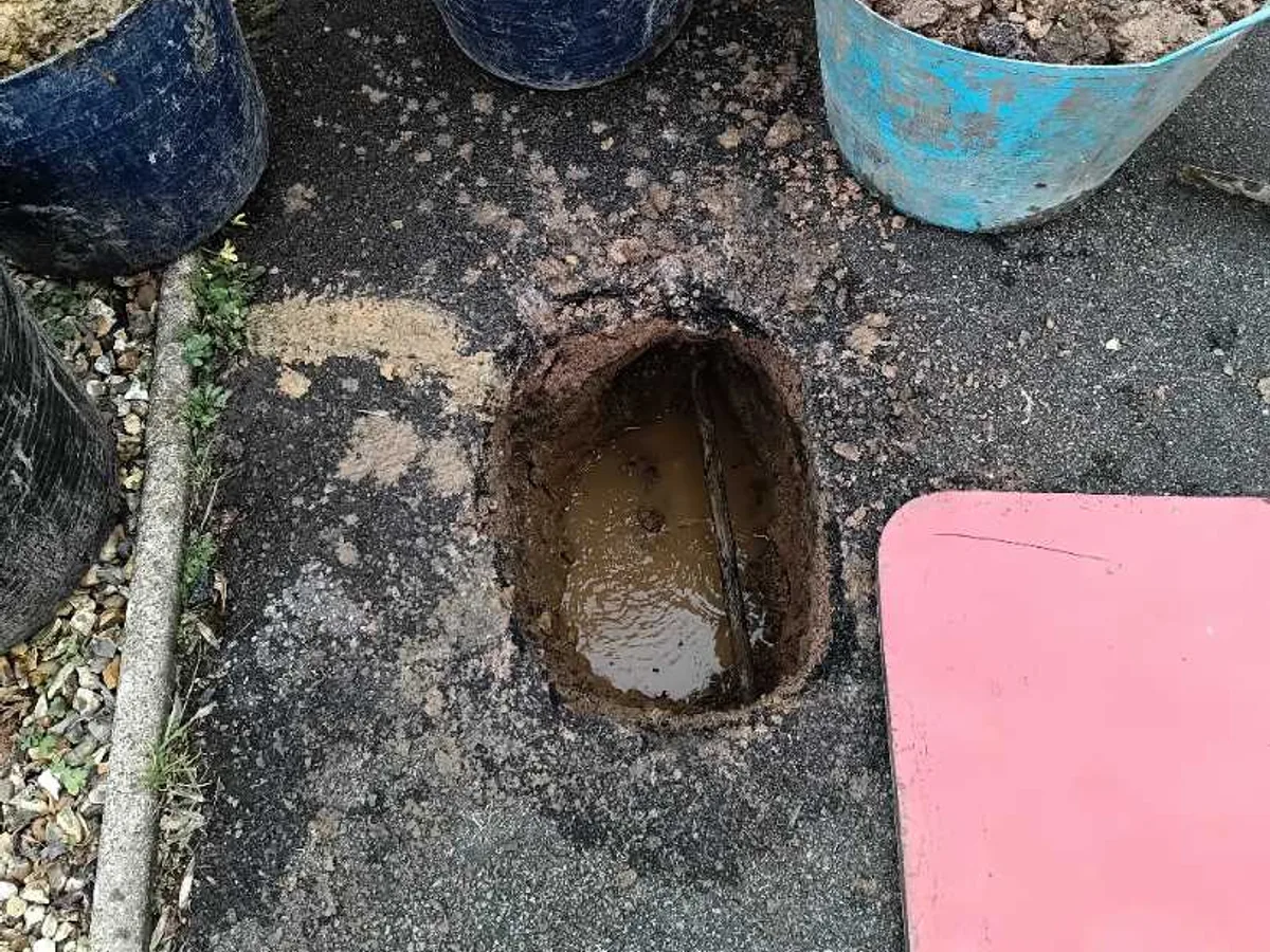 leak located at flooded excavation hole through tarmac driveway revealing buried pipe