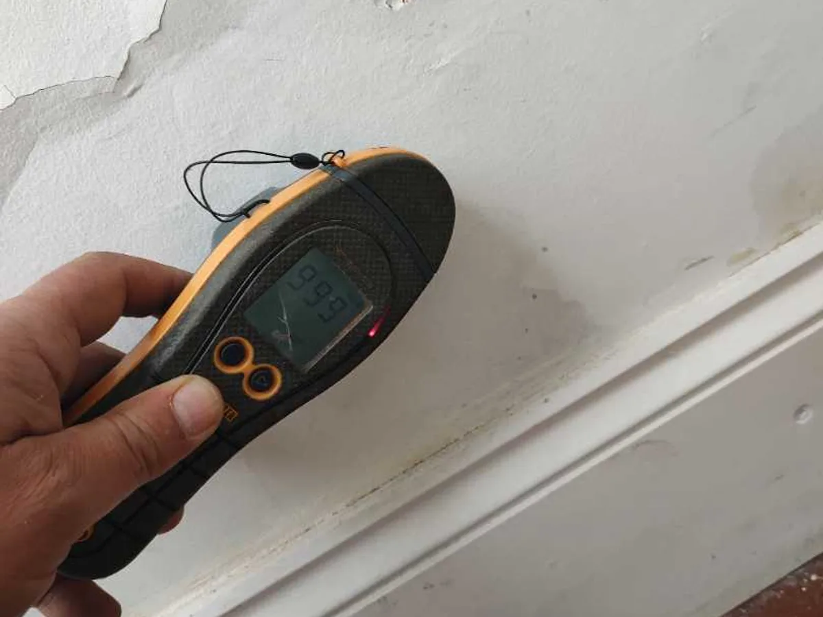 moisture meter held against hallway wall showing high damp reading during leak detection