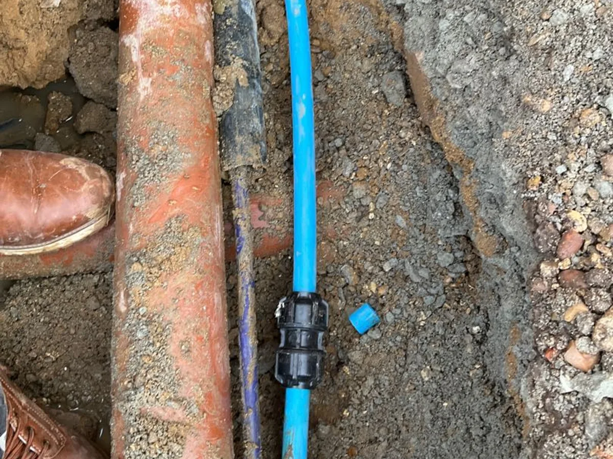 new blue MDPE pipe with compression coupling repair completed at exterior wall trench