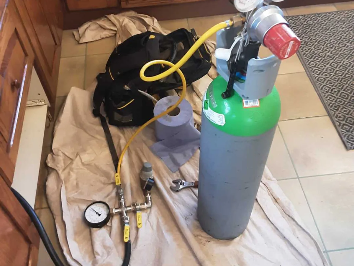 tracer gas cylinder and pressure gauge set up on kitchen floor during leak detection