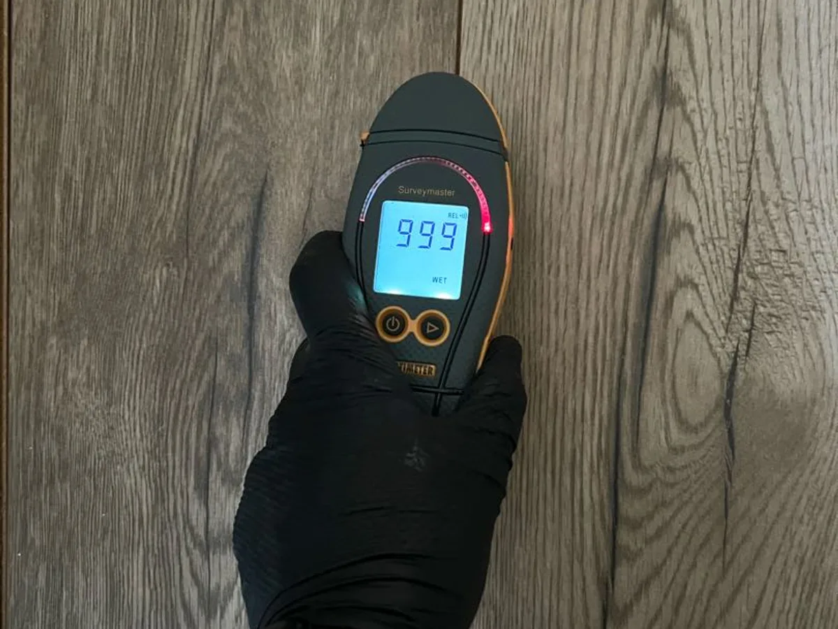 moisture meter displaying maximum reading of 999 on hallway floor during leak detection