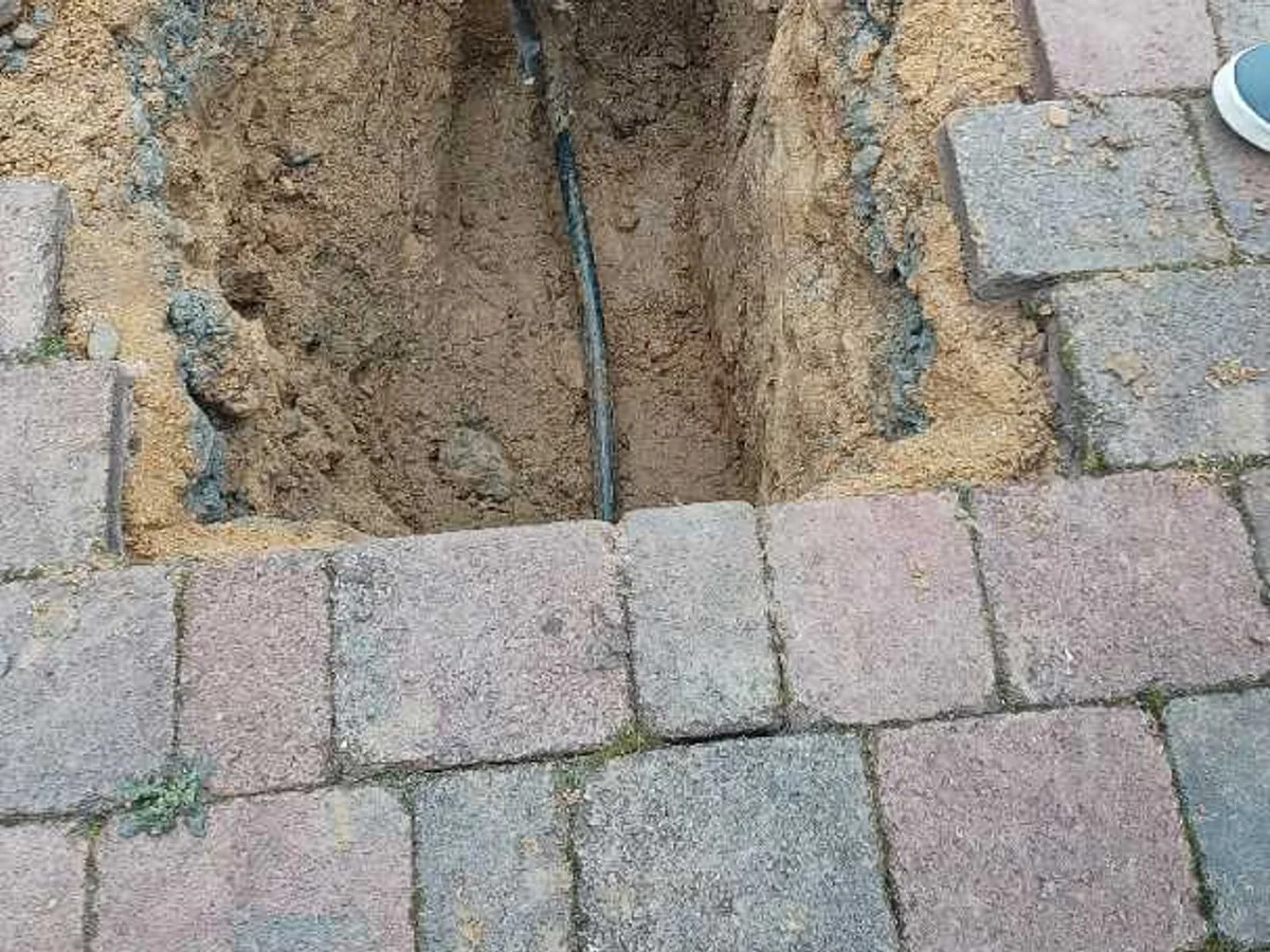 fault exposed at excavated trench revealing cracked black poly mains pipe beside manhole wall