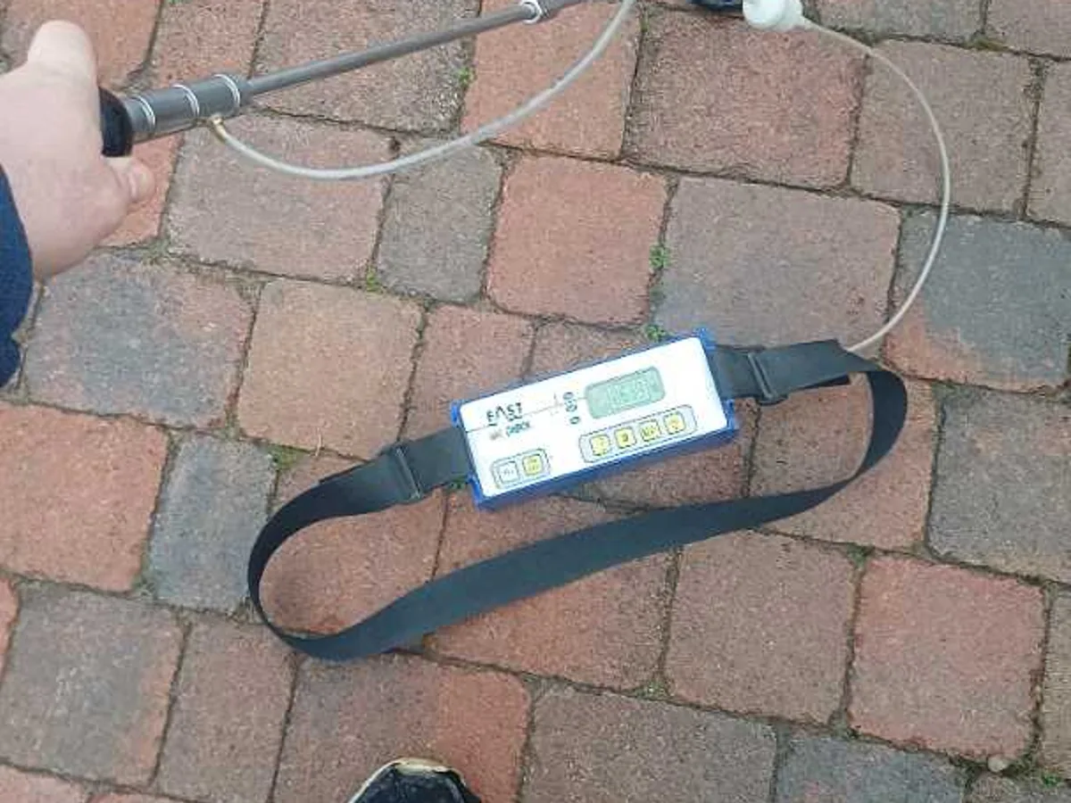 tracer gas detector probe held over block paving driveway during leak detection