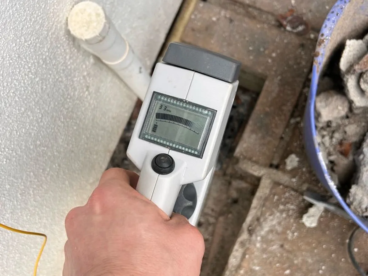 tracer cable reader held over exposed pipework while mapping pipe route during investigation — during leak detection