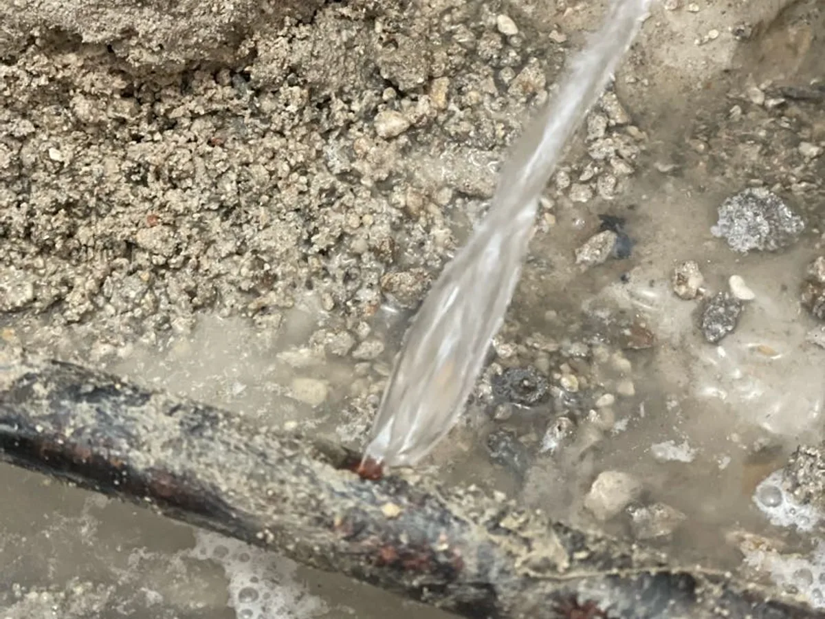 leak located at burst copper pipe below concrete slab with water flowing freely