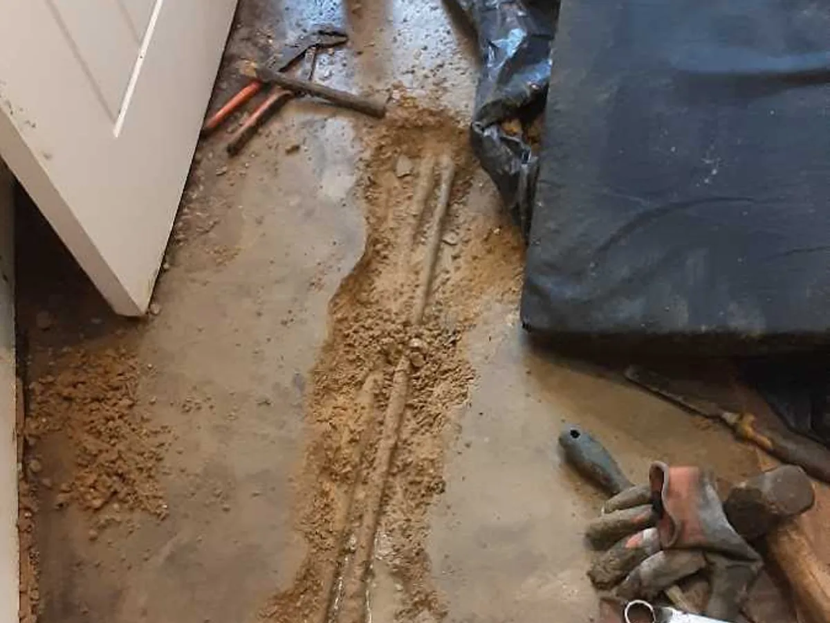 fault exposed at broken 15mm copper pipe in open concrete trench across utility room floor