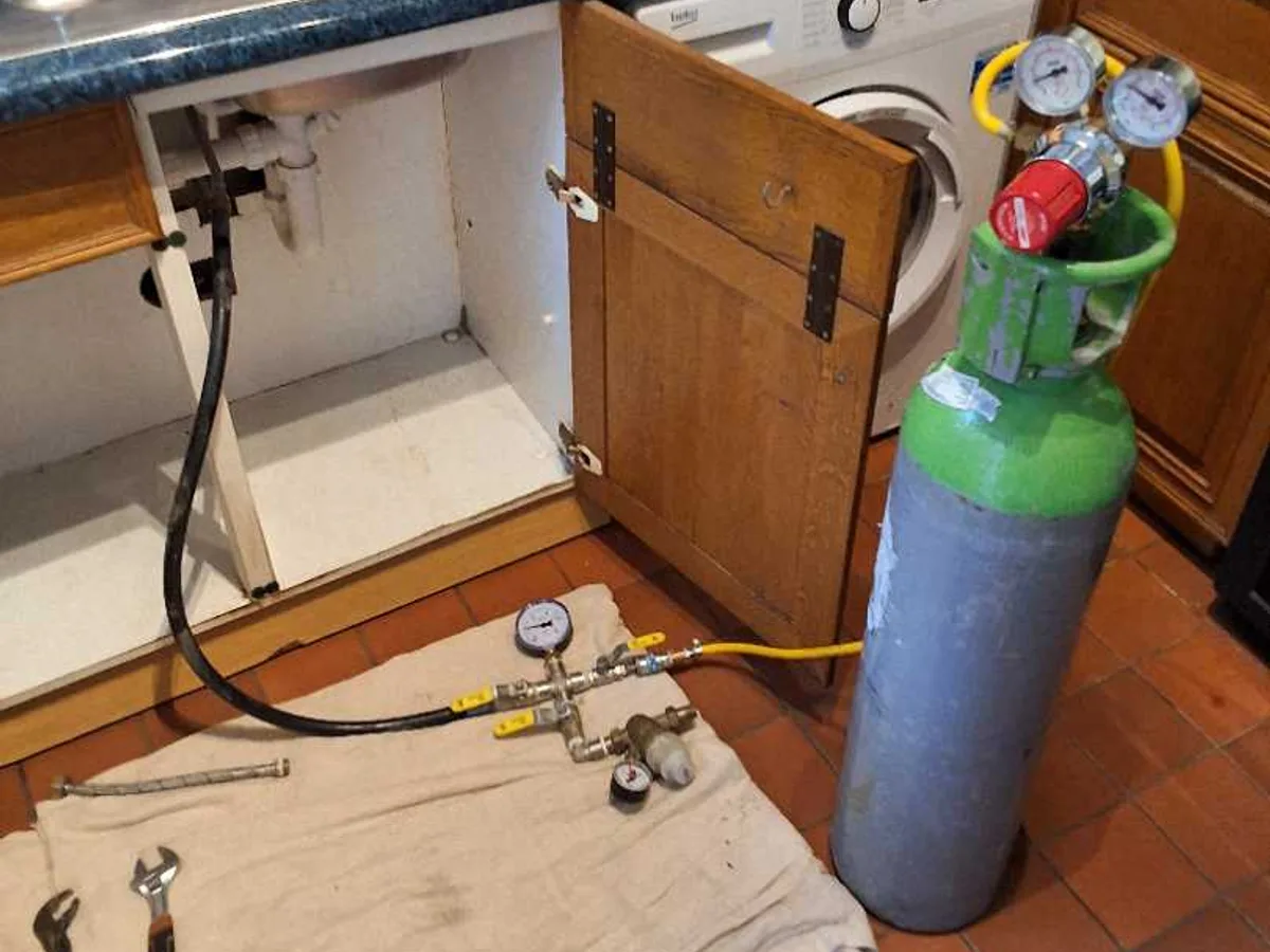 tracer gas cylinder and pressure test manifold connected to kitchen pipework during leak detection