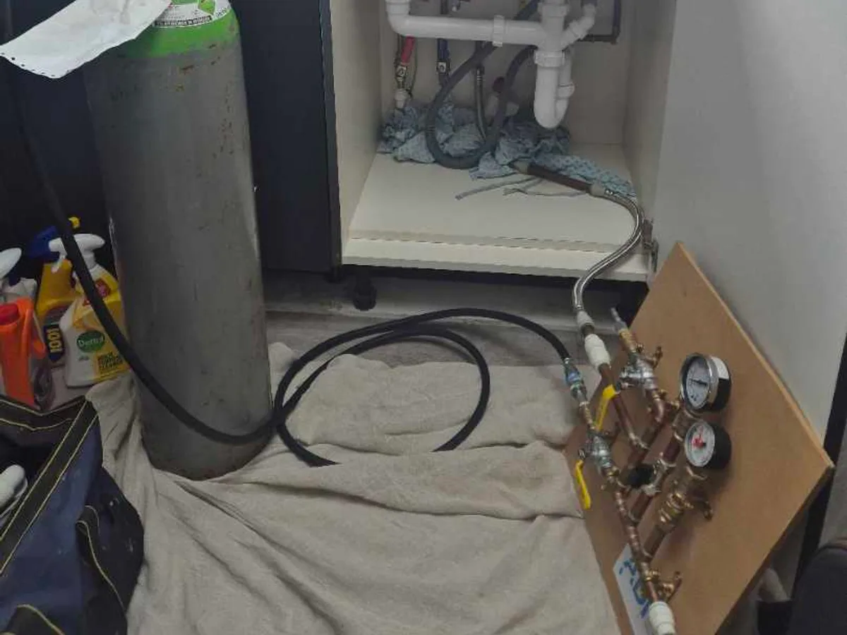 tracer gas cylinder connected under kitchen sink during leak detection