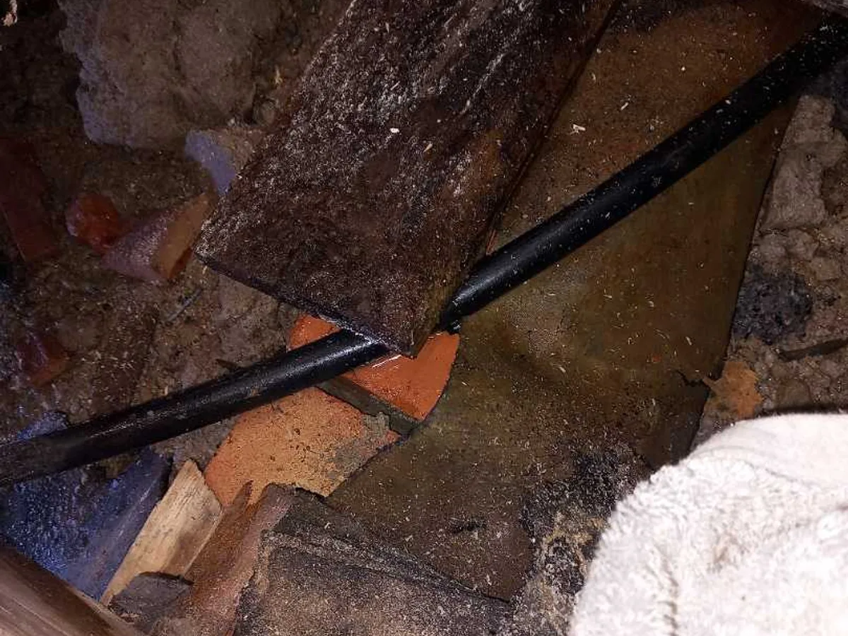 fault exposed at black plastic mains pipe surrounded by saturated debris beneath kitchen floor
