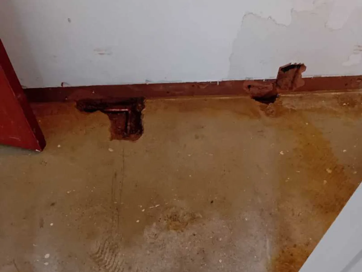 damp hallway floor with two excavation points visible at skirting board before works started