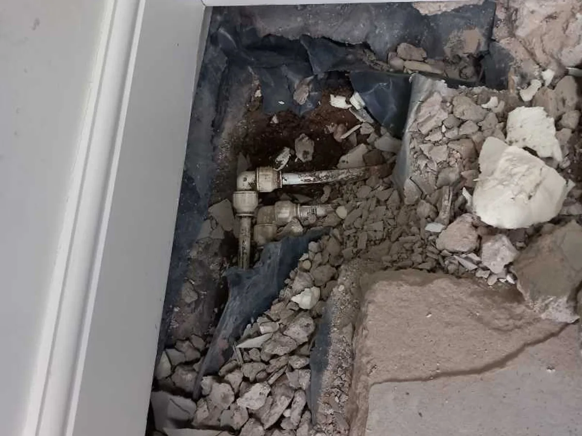 leak exposed at faulty plastic push-fit elbow fitting beneath broken concrete floor — leak located at