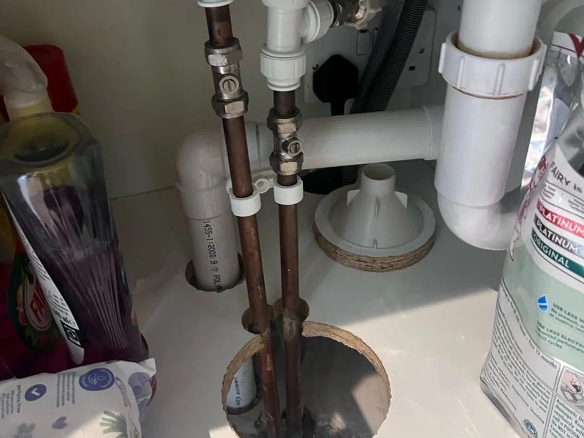 copper supply pipes and access hole beneath kitchen sink unit during leak detection