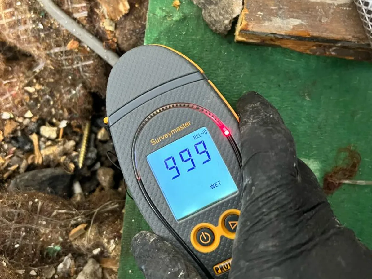 moisture meter displaying reading of 999 wet beneath bathroom floor during leak detection
