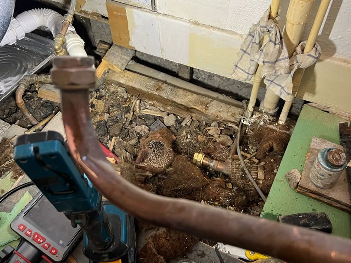 fault exposed at subfloor level showing corroded copper pipework and saturated debris beneath bathroom
