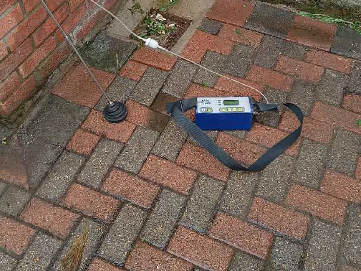 tracer gas detector unit on brick paving beside external pipework during leak detection