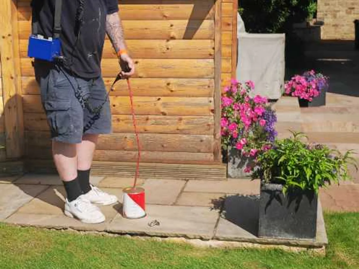 engineer using acoustic listening equipment on hardstanding near garden house during leak detection