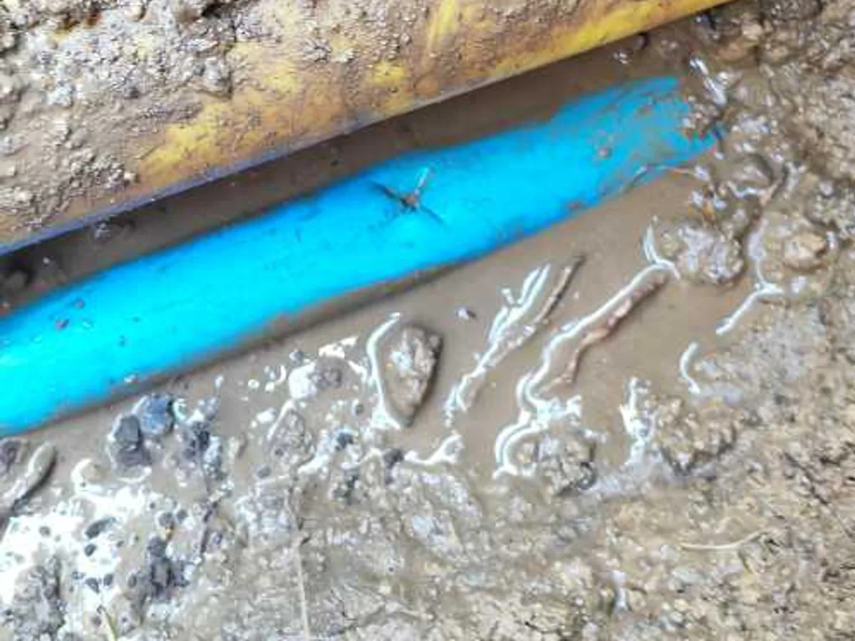 fault exposed at blue mains supply pipe with visible puncture hole and wet soil in excavation