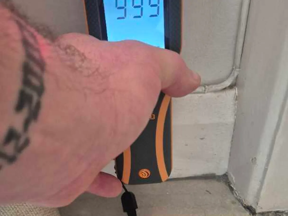 damp meter reading 999 held against skirting board during leak detection investigation