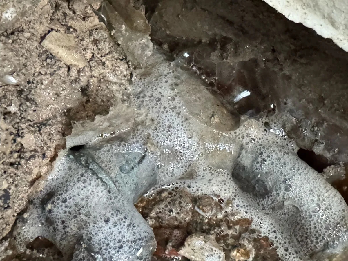fault exposed at saturated sub-floor ground with bubbling water pooling around buried pipework