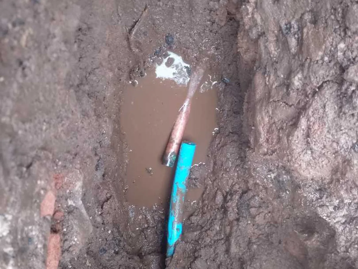leak located at flooded excavation showing blue mains pipe and copper connection beside water meter
