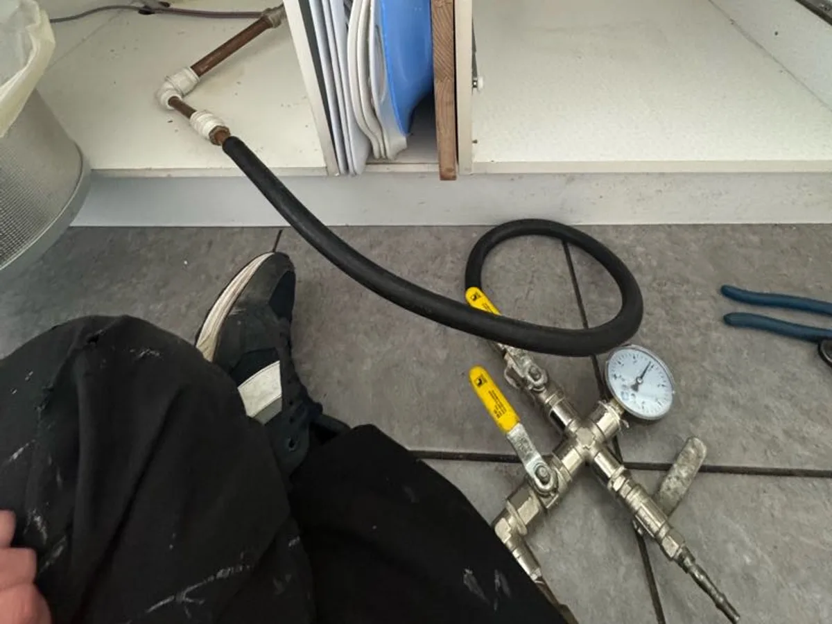 pressure gauge and hose connected under utility sink during leak detection