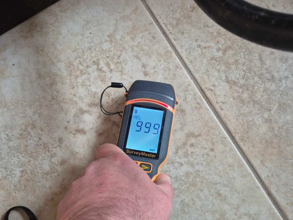 damp meter showing maximum 999 reading on kitchen floor tiles during leak detection