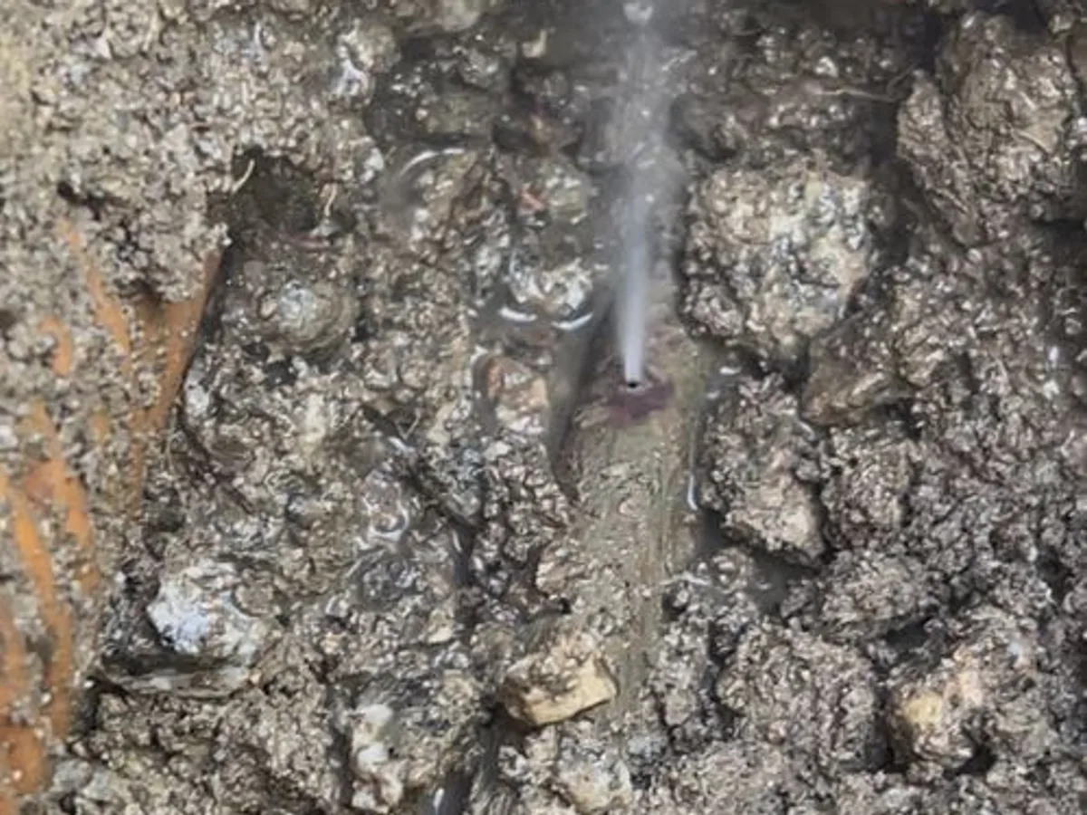 leak found at underground mains pipe with water jetting visibly from fault in exposed trench