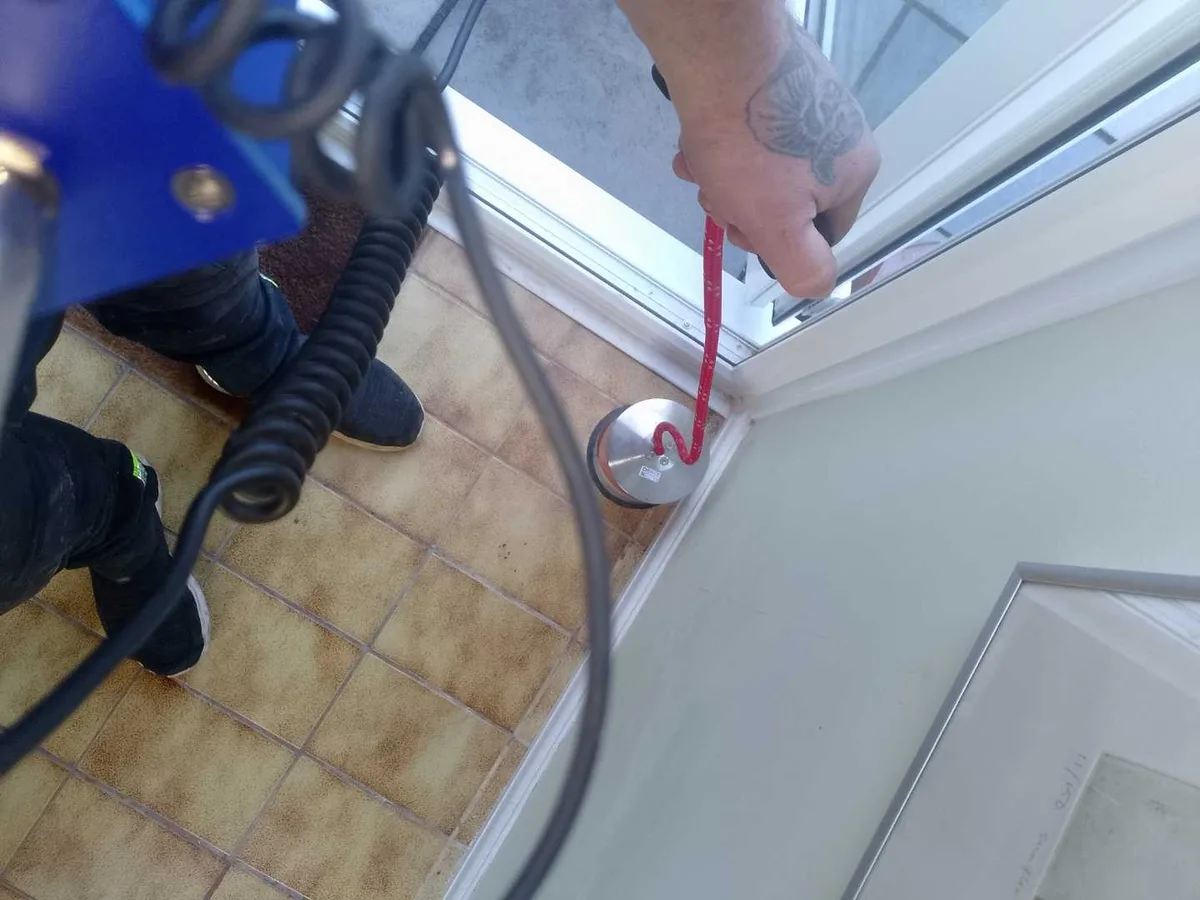 tracer gas detection probe held at porch floor threshold during leak detection survey