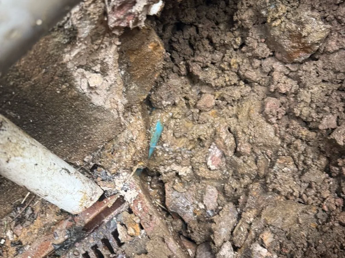 fault identified on 25mm blue MDPE mains supply pipe exposed in waterlogged soil beside drain — leak located at
