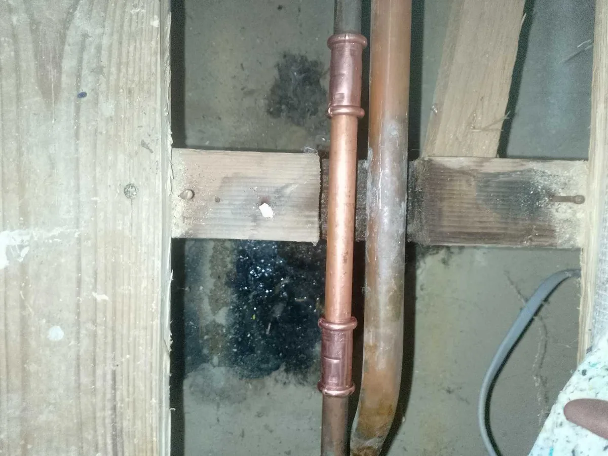 new copper pipe section with two press-fit couplings installed as repair completed beneath living room floor