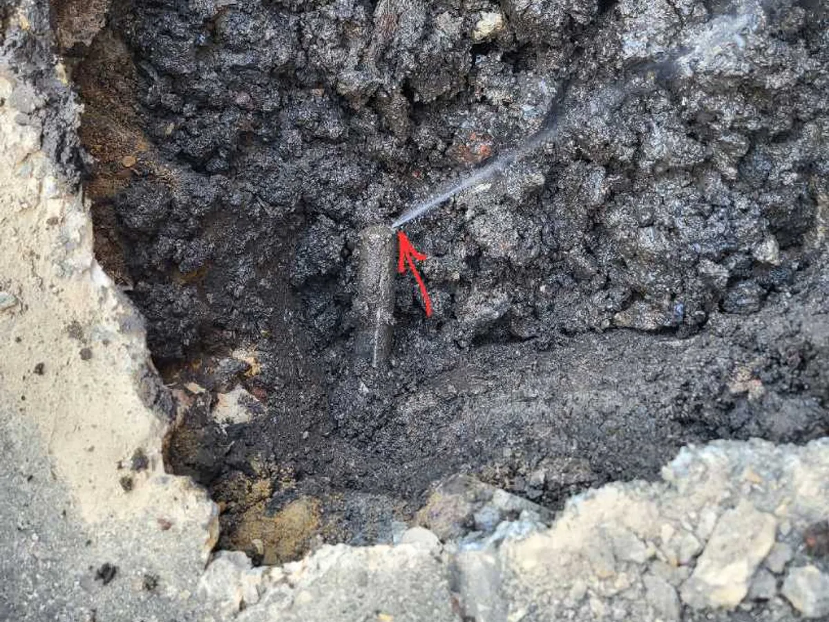 leak located at lead mains pipe with water jet visible in excavated trench beneath patio