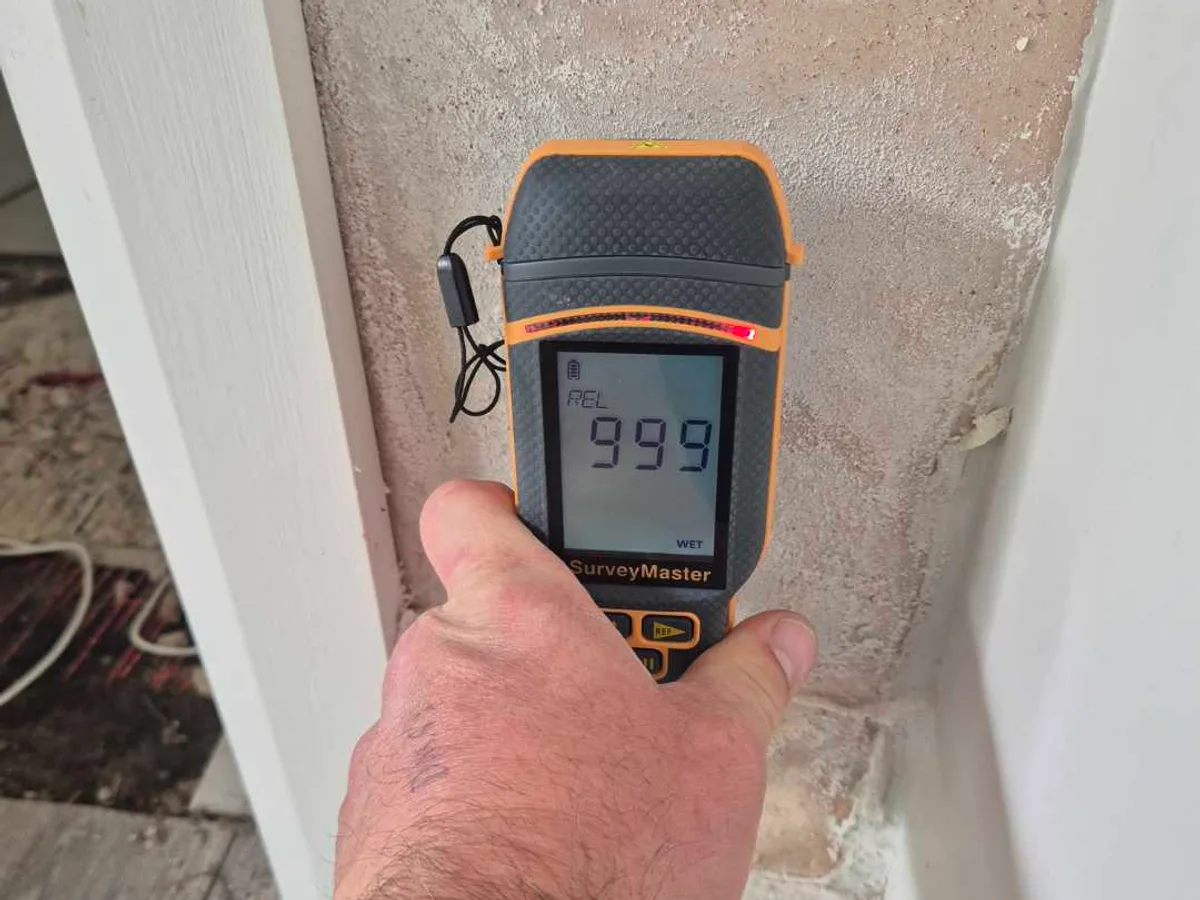 damp meter displaying maximum reading of 999 against saturated garden-room wall during leak detection