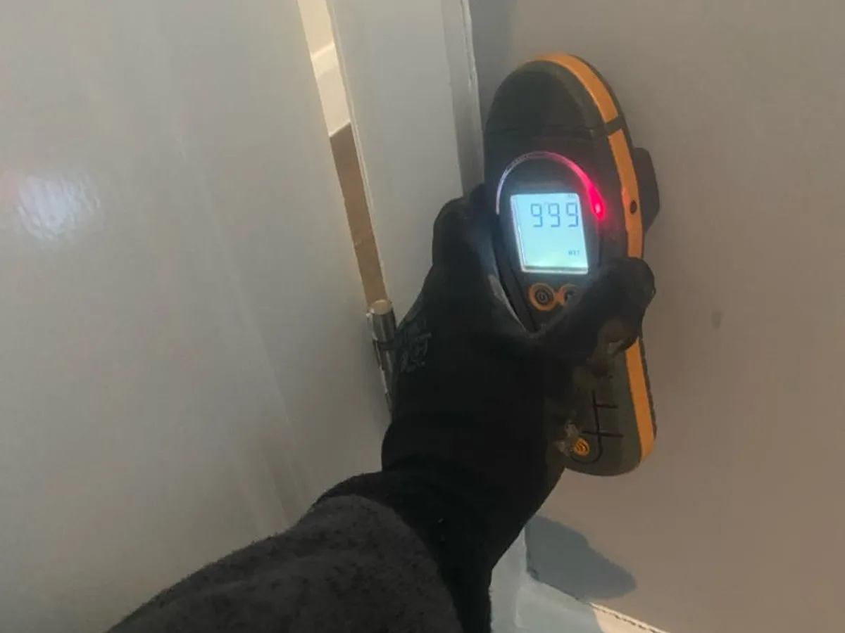 moisture meter reading 999 on lounge wall beside door during leak detection