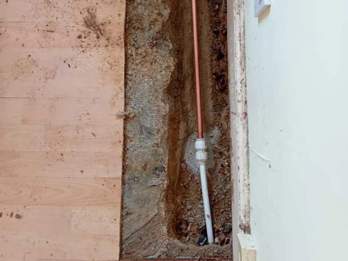 new copper pipe with compression coupling in kitchen floor trench after works completed