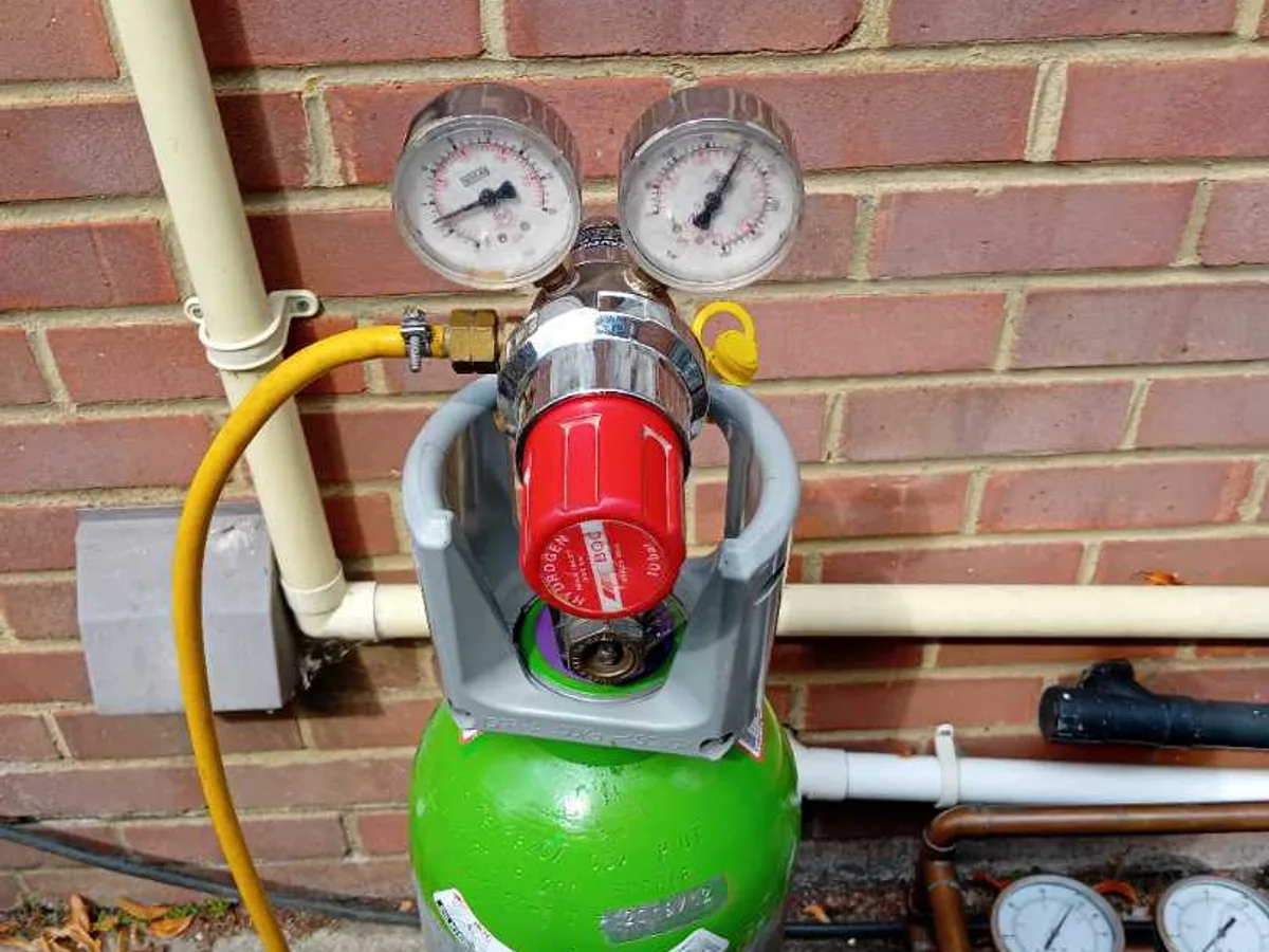 tracer gas cylinder with dual-gauge regulator connected to pipework during leak detection