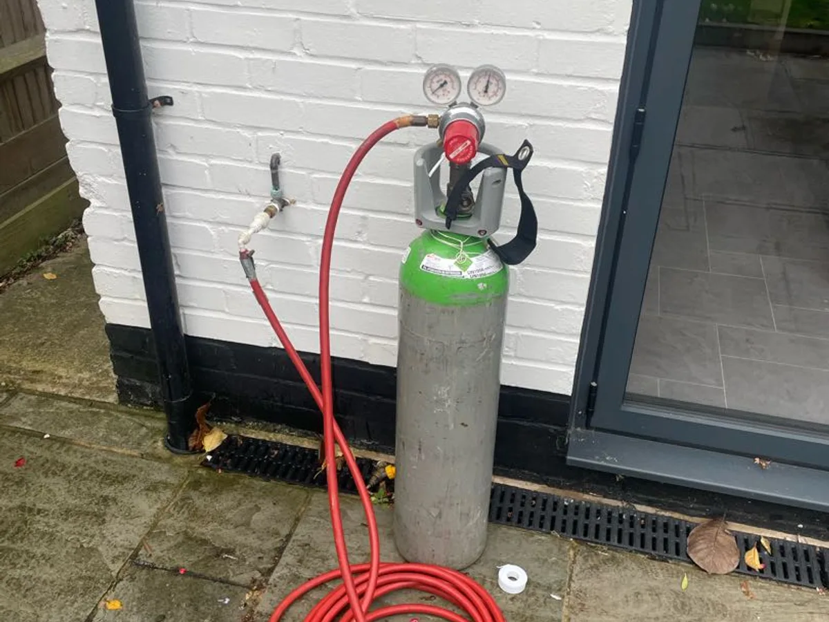 tracer gas cylinder connected to garden hose tap via red hose during leak detection