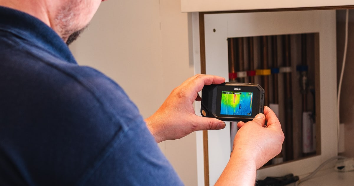 An ADI engineer using a thermal imaging camera to investigate pipework in a cupboard